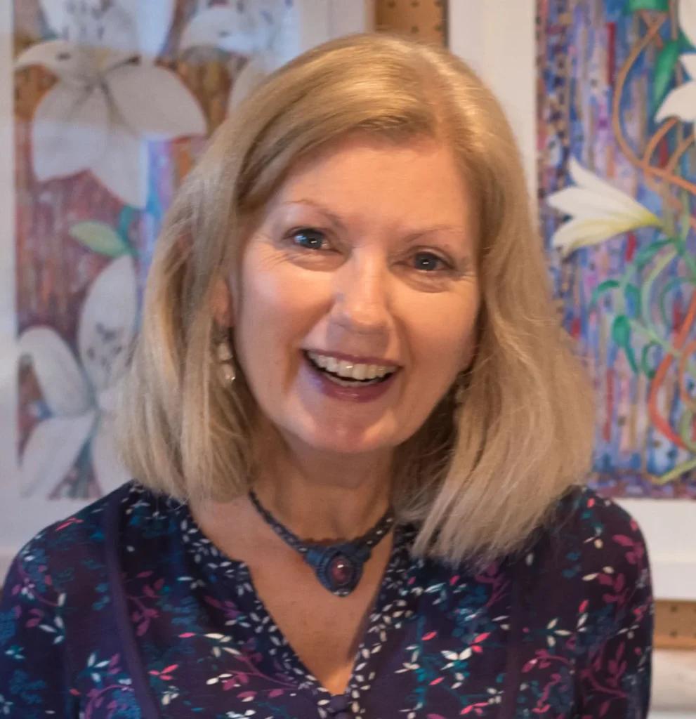 Portrait of Joan Hudson, Yorkshire artist, smiling warmly with colourful original paintings visible on the studio wall behind her